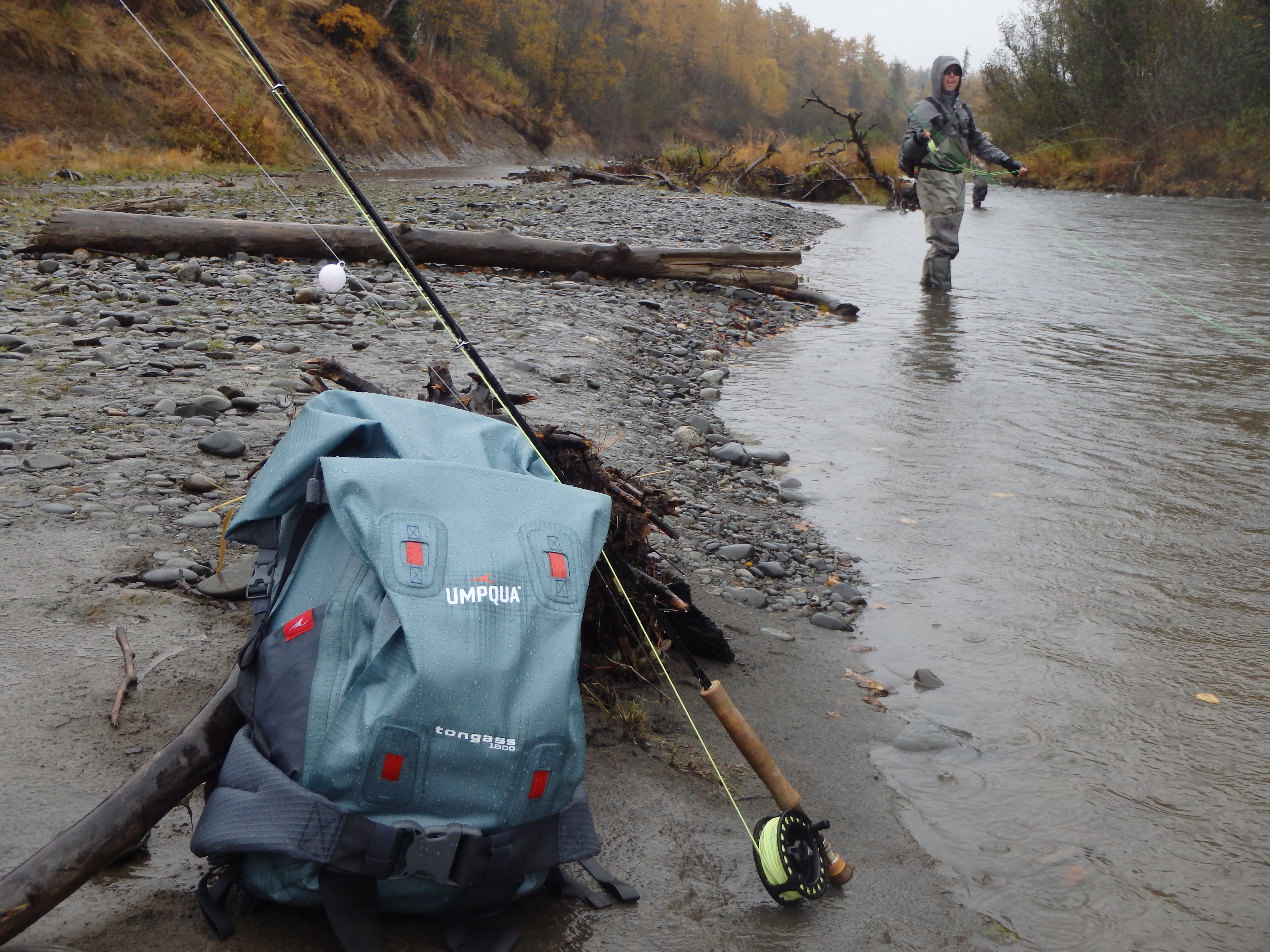 Pack and fly rod with angler fishing a river