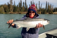 Angler holding a bright Steelhead with river view