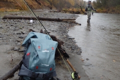 Pack and fly rod with angler fishing a river